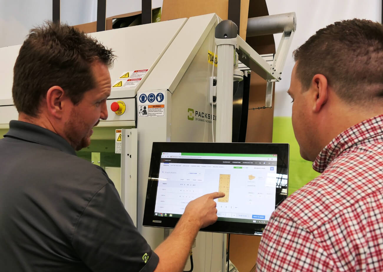 An image of two employees working with the touch screen interface of a Packsize machine at InterMetro.